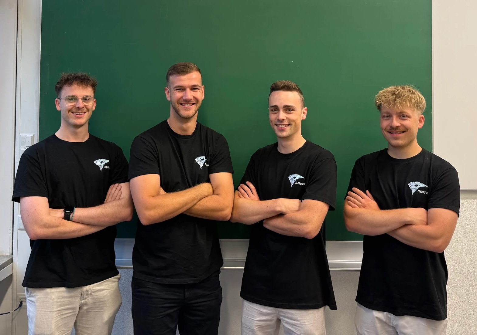 Das TERSUS-Team in schwarzen T-Shirts mit TERSUS-Logo vor einer Kreidetafel, von links nach rechts: Oliver Zimmermann, Hannes Eiberle, David Gitschier und Maximilian Wolf.
